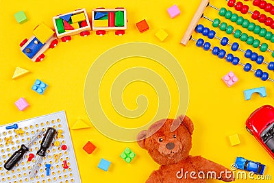 Kids toys background. Teddy bear, wooden train, colorful blocks, toy tools kit, cars, abacus on yellow background Stock Photo