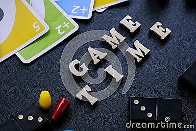 Kiev Ukraine - 10.03.21 Text GAME TIME spelled out in wooden letter. Surrounded by dice, dominoes uno playing cards on Editorial Stock Photo