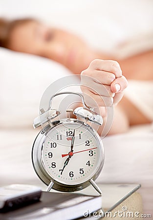 Killing her alarm. A young woman slamming her fist down on her alarm clock. Stock Photo