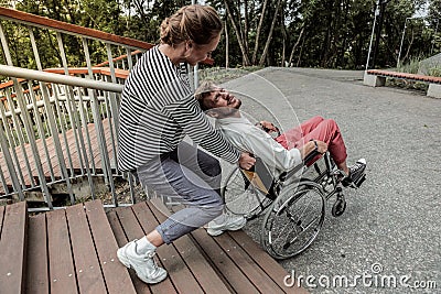 Kind girl helping to lift wheelchair with invalid Stock Photo