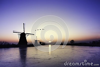 Kinderdijk - Geese flying over sunrise on the frozen windmills alignment Stock Photo