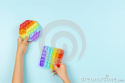 Kids hands holding colorful pop it fidget toys on blue background. Push pop-it fidgeting game for children Stock Photo