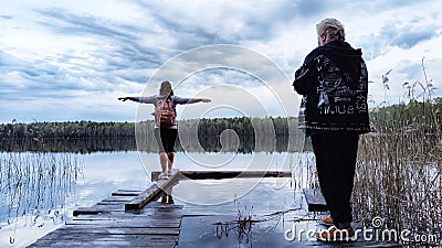 Kirov, Russia - April 29, 2023: Girls or women walks along old wooden pier with lake in background during evening and Editorial Stock Photo