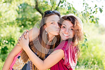 Kissing fun: brunette young women best friends having joyful time laughing & looking at camera on green su Stock Photo