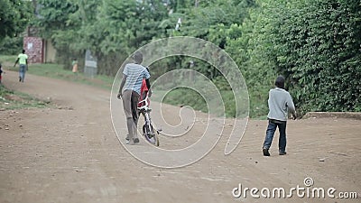 Kisumu, Kenia - 17. Mai 2018: Hintere Ansicht von den Jungen, die durch die Straße in Afrika gehen Mann mit Fahrrad gehend in Wal stock video Kisumu, Kenia - 17. Mai 2018: Hintere Ansicht von den Jungen, die durch die Straße in Afrika gehen Mann mit Fahrrad gehend in Wal stock video