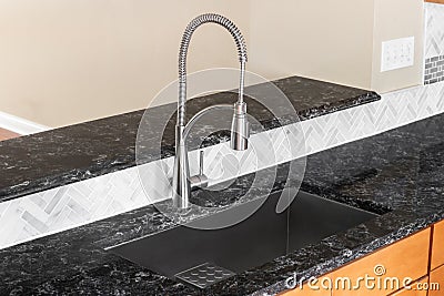 A kitchen faucet detail with a black marble countertop and herringbone backsplash. Stock Photo