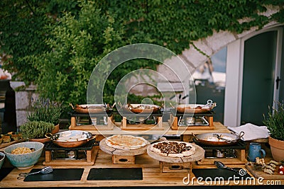 Kitchen with frying pans and wooden planks for serving pizza with food prepared for a banquet in the background of a Stock Photo