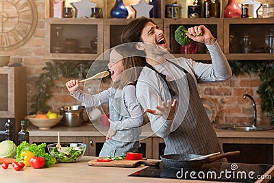 Kitchen Fun. Cheerful dad and his little daughter singing while cooking together Stock Photo