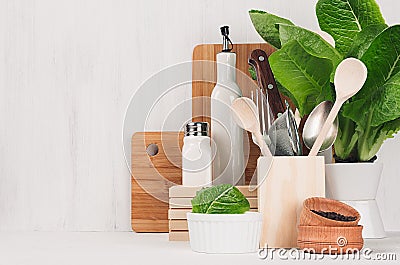 Kitchen modern decor - beige wooden utensils, brown cutting boards, green plant on soft light white wood background. Stock Photo