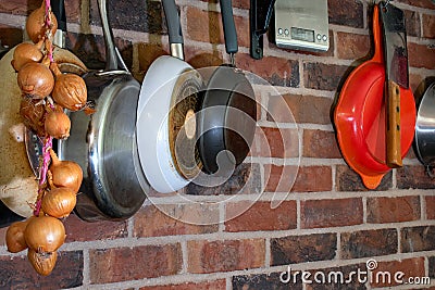 Kitchen utensils and pans hanging on a red brick wall. Onions and kitchen scales Stock Photo