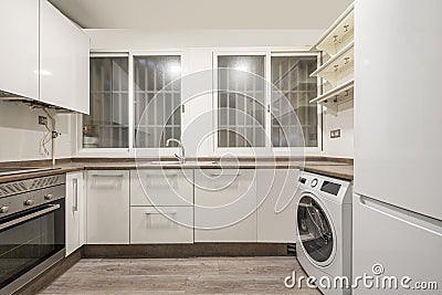 kitchen with white cabinets, brownstone worktops, twin barred windows and a white washing machine and fridge Stock Photo