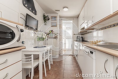 A kitchen with white furniture and wooden details, integrated white appliances, access to a terrace and a folding dining table Stock Photo