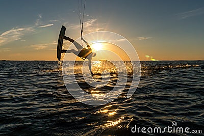 Kitesurfer doing handslide in sunset with sunstar and silhouette Stock Photo