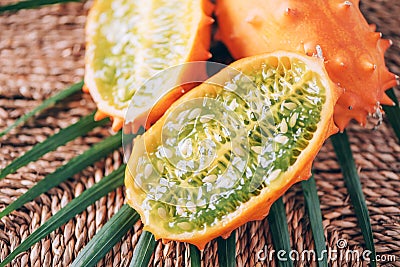 Kiwano or african horned melon with palm leaves on rattan background. Cutted hedged gourd, african horned cucumber, english tomato Stock Photo