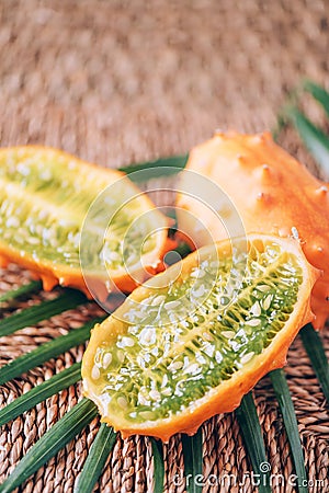 Kiwano or african horned melon with palm leaves on rattan background. Cutted hedged gourd, african horned cucumber, english tomato Stock Photo