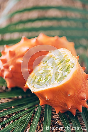 Kiwano or african horned melon with palm leaves on rattan background. Cutted hedged gourd, african horned cucumber, english tomato Stock Photo