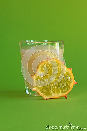 Kiwano slice, exotic vegetable cucumis metuliferus and a glass of fruit juice on a green background. Soft focus. Vegetarian food Stock Photo