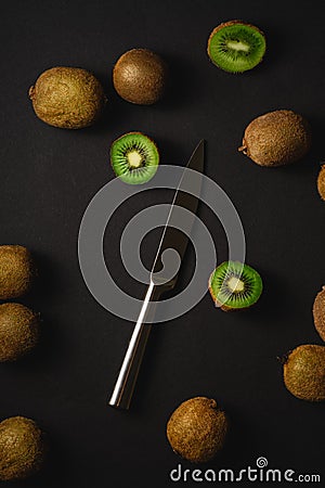 Kiwi fruits half sliced with kitchen knife on dark black moody plain background Stock Photo