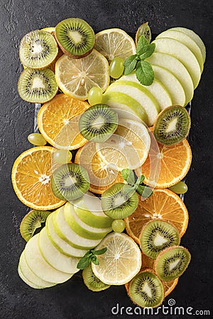 Kiwi, orange slices, green grapes, Apple, mint sprig , fresh citrus on a black background, square shape, top view Stock Photo