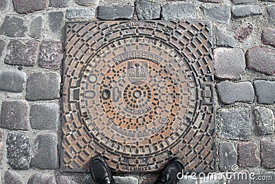 KLAIPEDA, LITHUANIA - JUNE 22, 2013: Sewer metal round hatch on pavement stone surface Editorial Stock Photo
