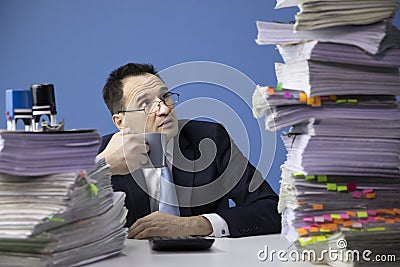 Knackered office employee looks frightened at high stack of documents Stock Photo