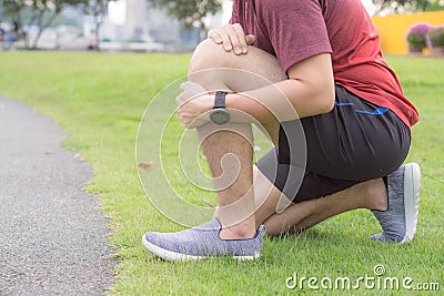 Knee Injuries. Young sport man holding knee with his hands in pain after suffering muscle injury during a running workout at park Stock Photo