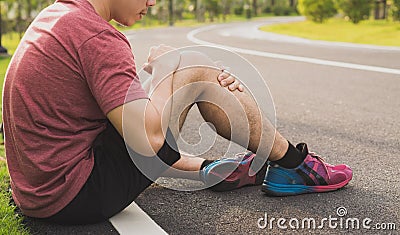 Knee Injuries. Young sport man holding knee with his hands in pain after suffering muscle injury during a running workout at park Stock Photo