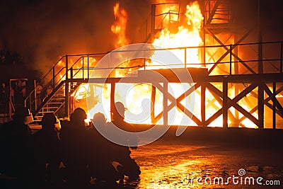 Kneeling firefighters in front of burning structure during firefighting exercise Editorial Stock Photo