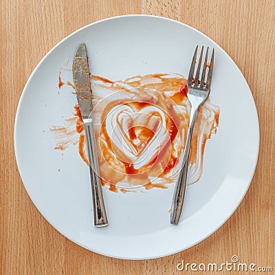 Knife and fork over in finish plate and heart shape ketchup. Stock Photo