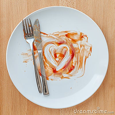 Knife and fork over in finish plate and heart shape ketchup. Stock Photo