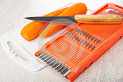 Knife and peeled carrots on cutting board, orange color grater on wooden table Stock Photo