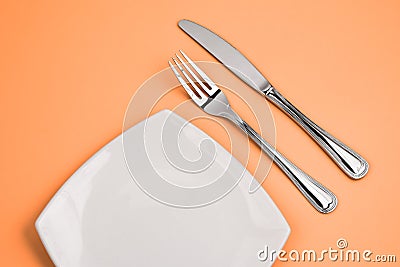 Knife, square white plate, fork on pink top view Stock Photo