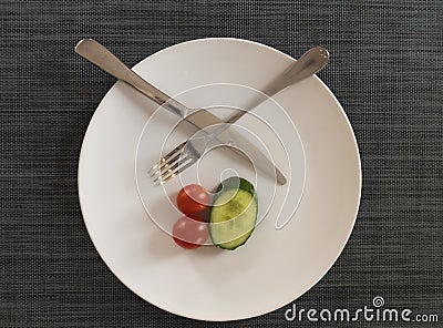 Knife, white plate and fork on gray background. A liittle of vegetables on the plate, diet Stock Photo