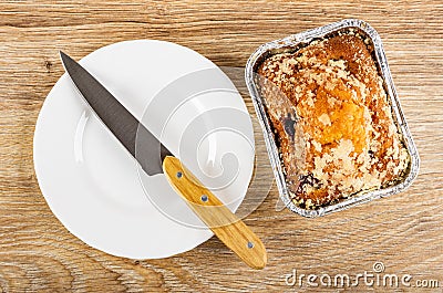 Knife on white plate, muffin with raisin in foil mold on wooden table. Top view Stock Photo