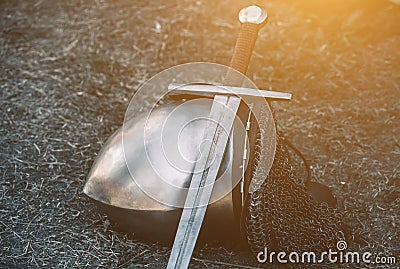 Knight`s helmet and shiny metal lying on the ground, it put an old steel sword with leather handle Stock Photo