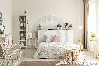 Knit blanket in basket standing on dirty pink carpet in real photo of bright feminine bedroom interior with Stock Photo