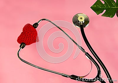 Knitted red heart with a phonendoscope on a pink background. Heart disease patient support concept Stock Photo