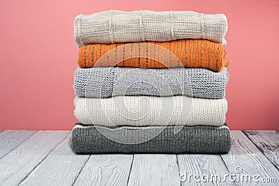 Knitted wool sweaters. Pile of knitted winter clothes on red wooden background, sweaters, knitwear, space for text. Stock Photo