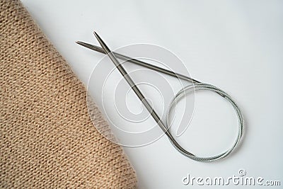 Knitting beige fabric on a white background with knitting steel needles. Copyspace. For for yarn stores, needlework, banner design Stock Photo
