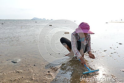 Ko Phangan, Thailand, March 15, 2022: octogenarian woman seek clams on the sea Editorial Stock Photo