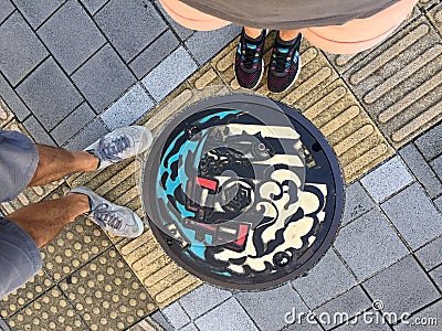 Top view of male and female legs standing in front of a Japanese manhole Editorial Stock Photo