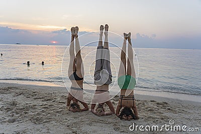 Three young girl practice yoga headstand asana on sea shore at sunset on the tropical island of Koh Phangan, Thailand Editorial Stock Photo