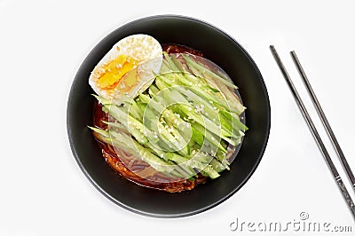 Korean cold noodles with spicy sauce, topped with cucumber, boiled egg and crushed sesame seeds in a black bowl. Stock Photo