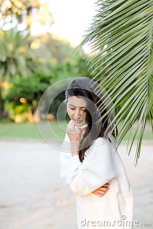 Korean dreaming girl in white sweater standing near palm leaf. Stock Photo