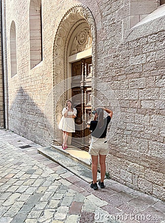 Kotor, Montenegro - 06 august 2023: Girl-photographer photographs a bride standing near the arched door of an old church Editorial Stock Photo