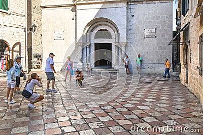 Tourists play with a cat as a beggar asks for money on the steps of the St Nicholas Church in Kotor Montenegro Editorial Stock Photo