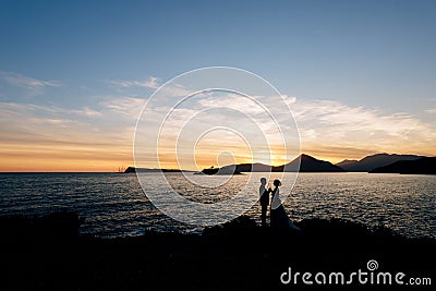 Kotor, Montenegro - 08.06.17: Silhouettes of newlyweds stand holding hands on the beach near the sea on the background Editorial Stock Photo