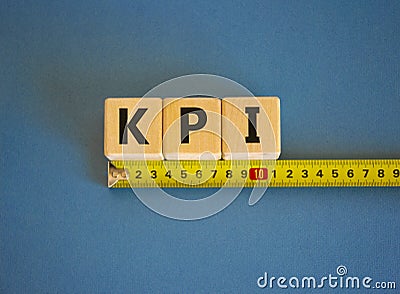 KPI - key perfomance indicator symbol. The word KPI, key perfomance indicator on cubes arranged behind the ruler on beautiful blue Stock Photo