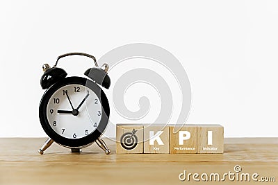 KPI, Key Performance Indicator, and dartboard icon on wooden cube with black analog alarm clock on desk Stock Photo