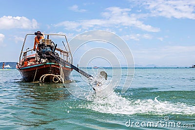 Krabi, Thailand - February 12, 2019: The driver of a longtail motorboat drives a motor with a long drive and a propeller. Sailor Editorial Stock Photo